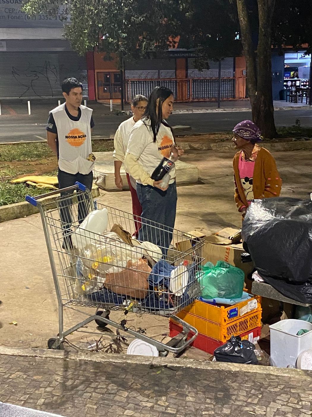 Voluntários conversando com uma senhora ao lado do carrinho com as coisas dela