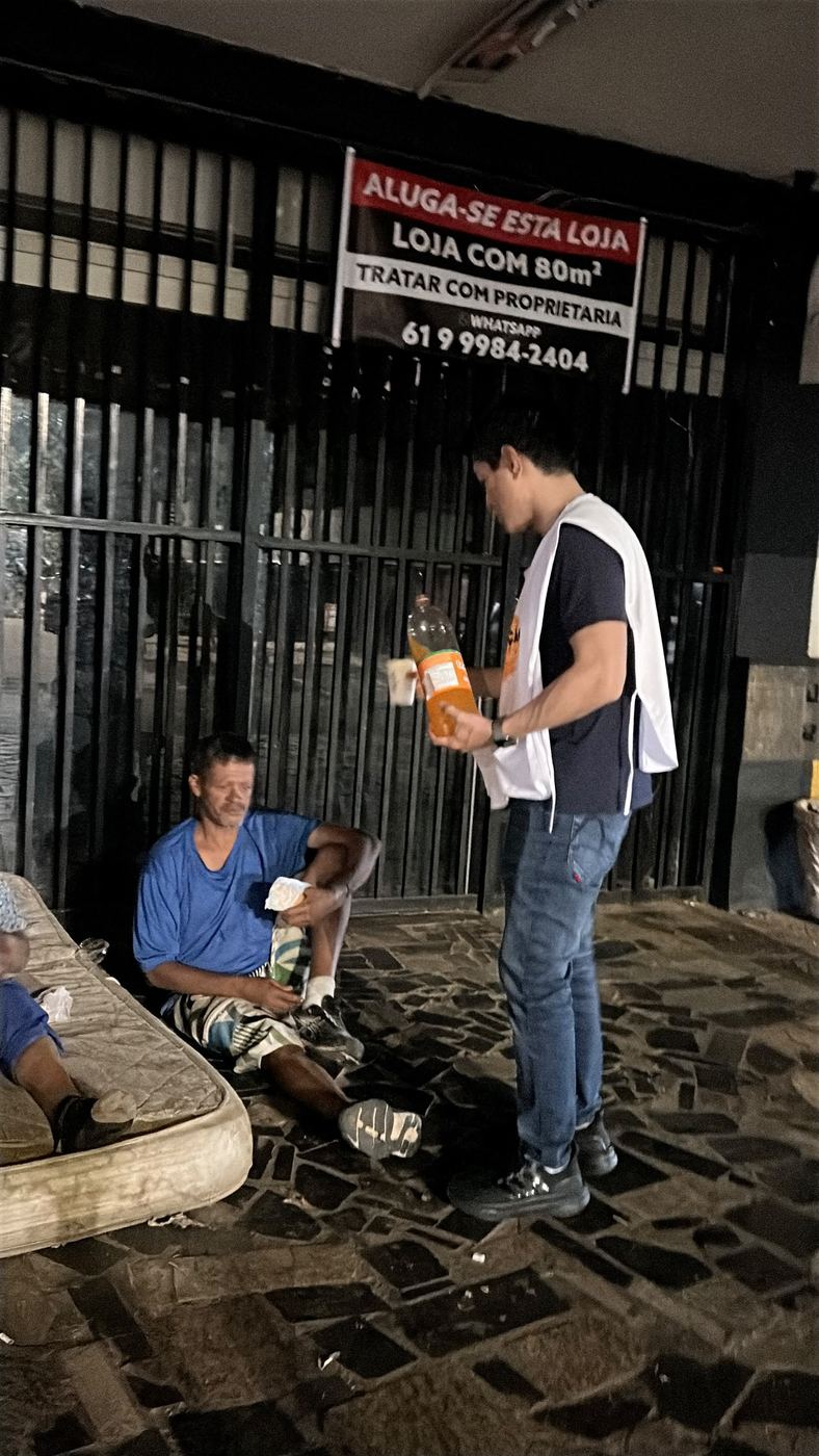 Voluntário entregando comida a um homem sentado em frente à loja fechada