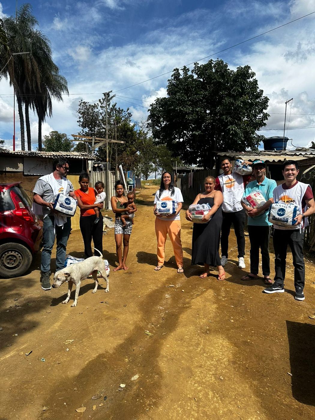 Voluntários e famílias segurando cestas básicas em rua de terra