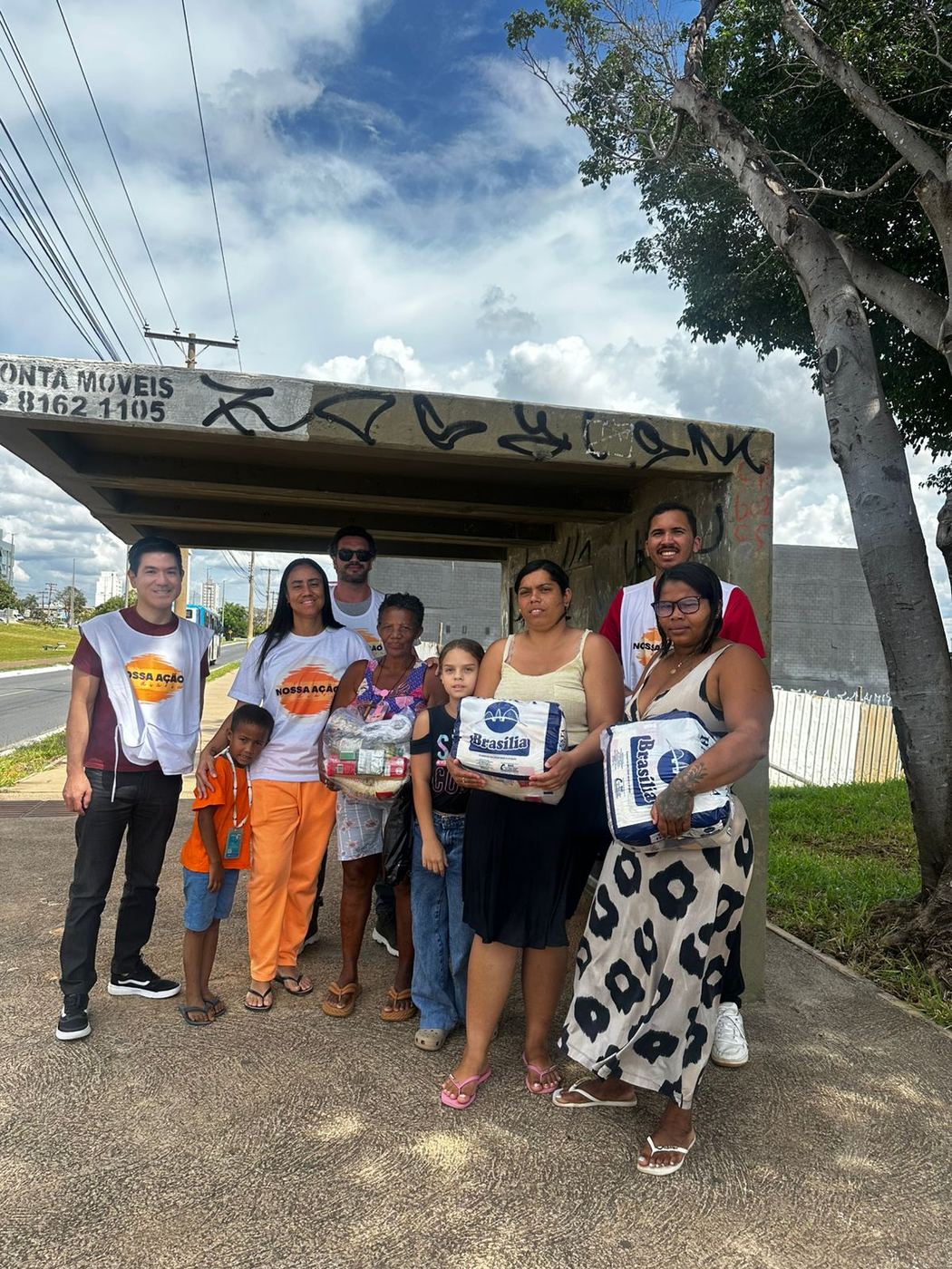 Roberta e voluntários com famílias que receberam cestas e fraldas, num ponto de ônibus