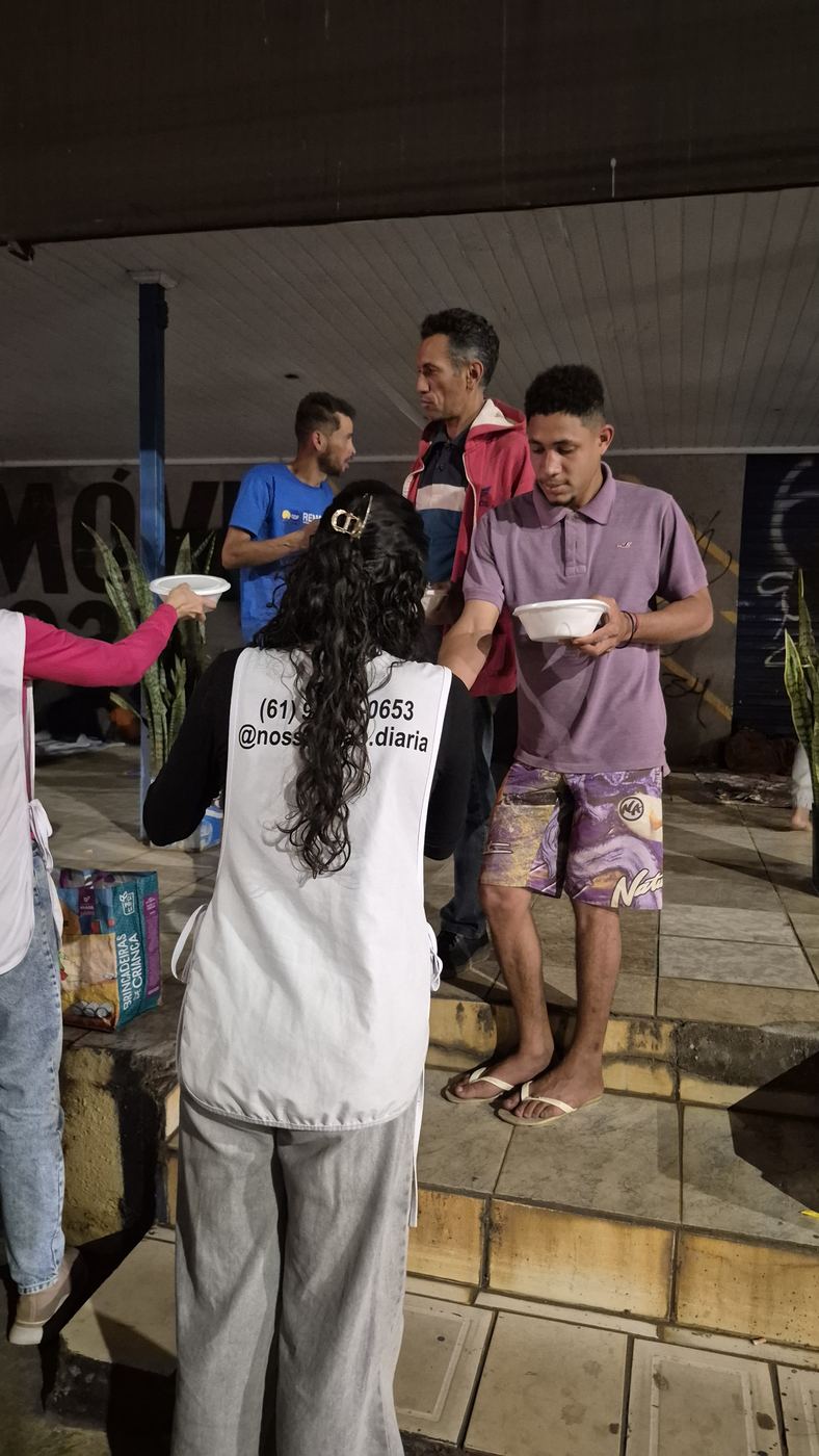 Voluntária entregando prato de comida para jovens na calçada
