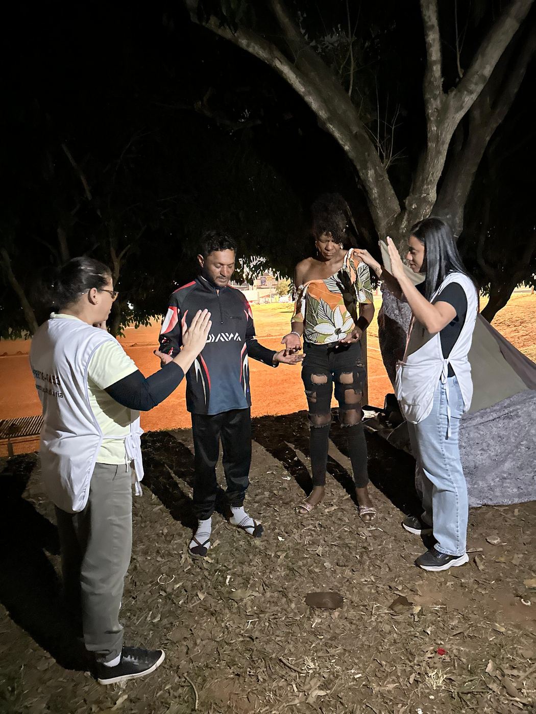 Voluntários orando de mãos dadas com pessoas na rua à noite