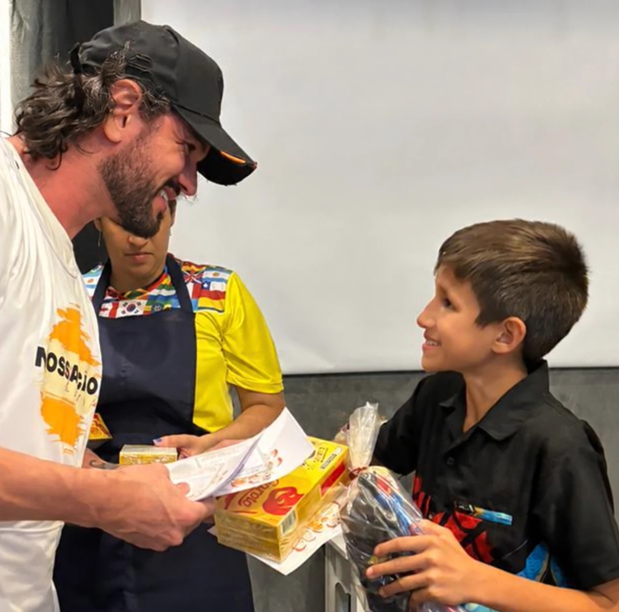 Voluntário sorrindo ao entregar um kit para um menino