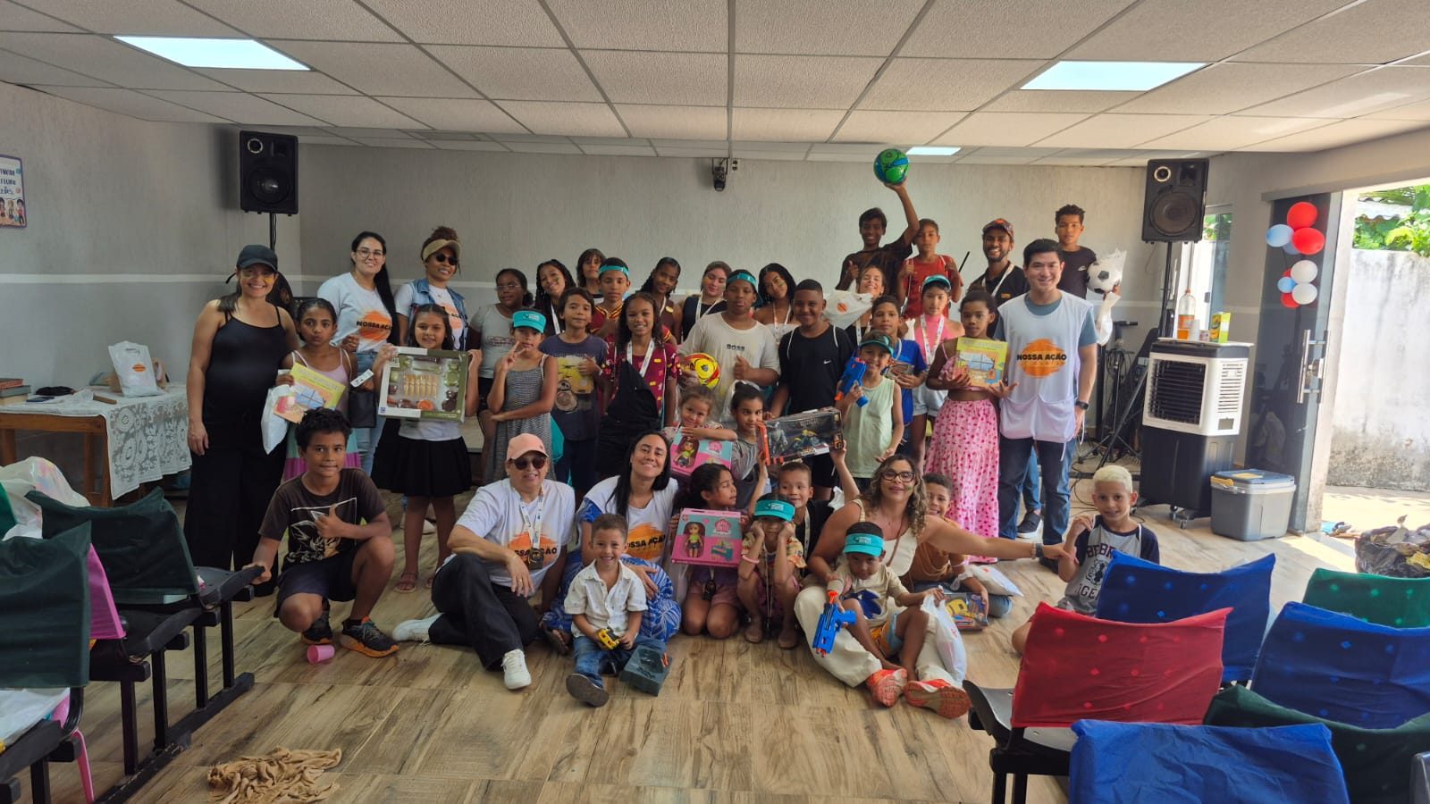 Crianças e voluntários reunidos no salão com os brinquedos recebidos no Dia das Crianças